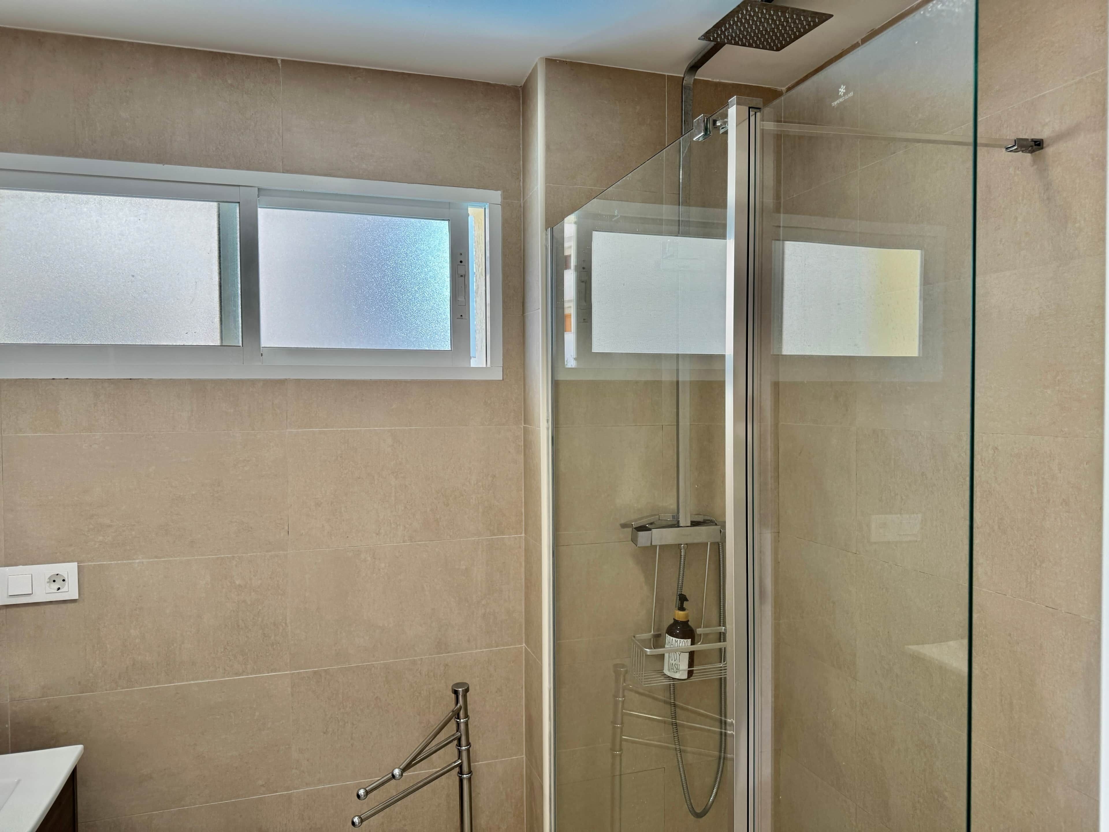 Un bagno moderno con doccia vetro, una finestra e un porta asciugamani.