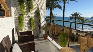 A balcony with wicker furniture, potted plants, and a view of the ocean. - 0. Skol Marbella 111A (Marbella)