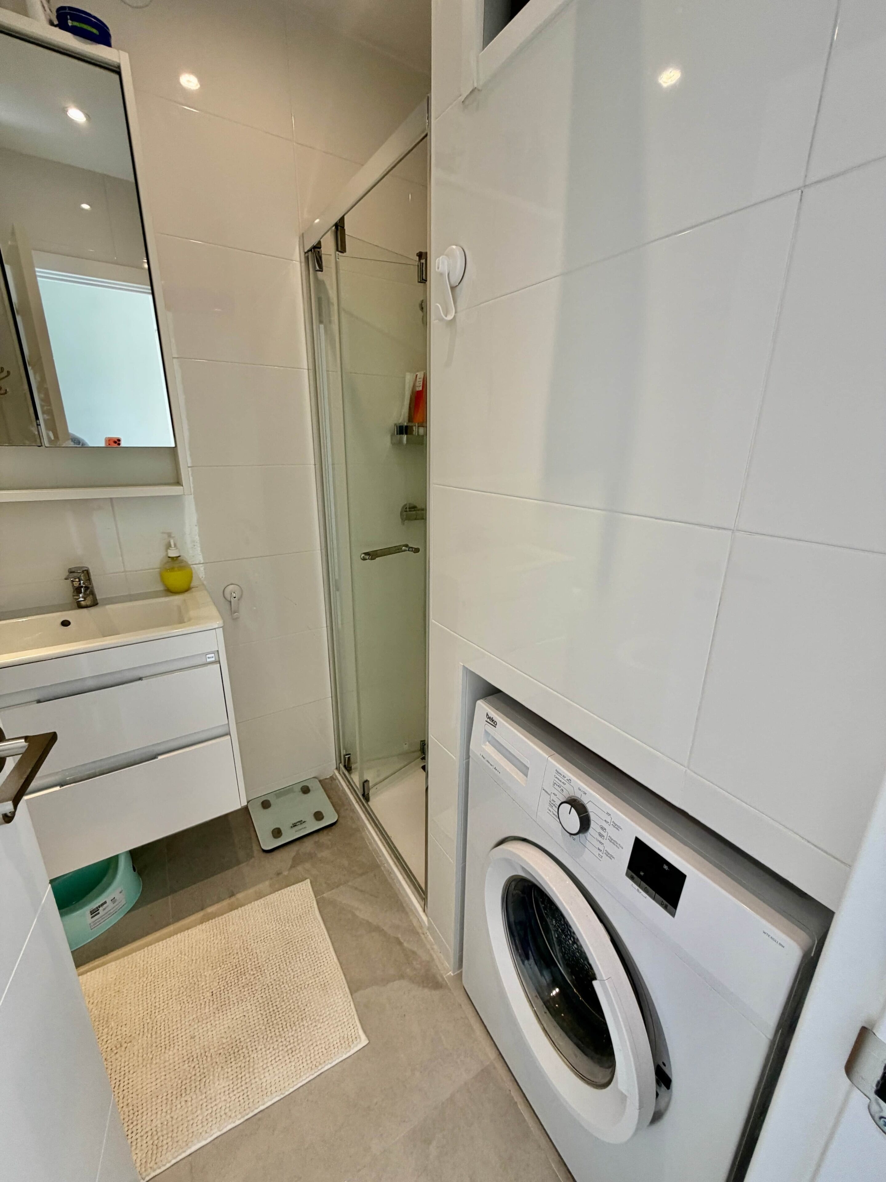 A modern bathroom with a glass shower, a washing machine, and a sink with a mirror above it.