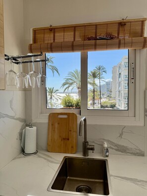 A kitchen with a window view, a wooden cutting board, a roll of paper towels, and a metal sink. - 0. Skol Marbella 111A (Marbella)