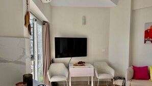 A modern living room with a flat-screen TV, two chairs, a small table, a sofa, and a window with curtains. - 0. Skol Marbella 111A (Marbella)