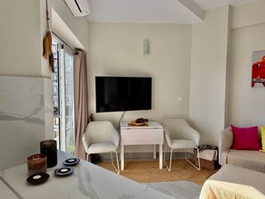 A modern living room with a flat-screen TV, two chairs, a small table, a sofa, and a window with curtains. - 0. Skol Marbella 111A (Marbella)
