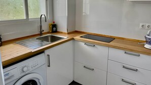 Kompakti keittiö, jossa on ruostumattomasta teräksestä valmistettu pesuallas, astianpesukone, puutasot ja valkoiset kaapit.