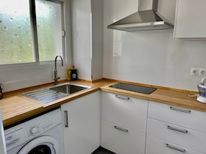 Eine kleine Küche mit Spüle aus Edelstahl, Geschirrspüler, Holz Arbeitsplatten und weißen Schränken.