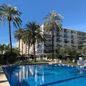 Ein Schwimmbecken mit Palmen und einem mehrstöckigen Hotel im Hintergrund.