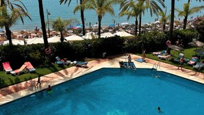 Ein Schwimmbecken mit Schwimmern und Sonnenanbetern, umgeben von Palmen und Strandsonnenschirmen.