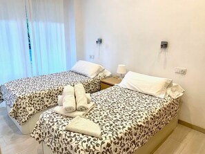 Ein Hotelzimmer mit zwei Betten, einem Nachttisch, einer Lampe und einem Fenster mit Vorhängen.