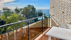 Un balcón con vistas al mar, una mesa blanca y un muro de ladrillo.