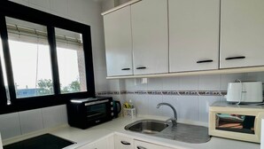 Cocina compacta con armarios blancos, un tostador negro, un lavamanos y una ventana con persianas.