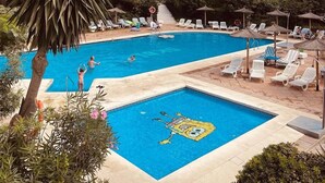 Una piscina con diseño de personaje de caricatura, rodeada de sillas de descanso y sombrillas, con un edificio de varios pisos al fondo.
