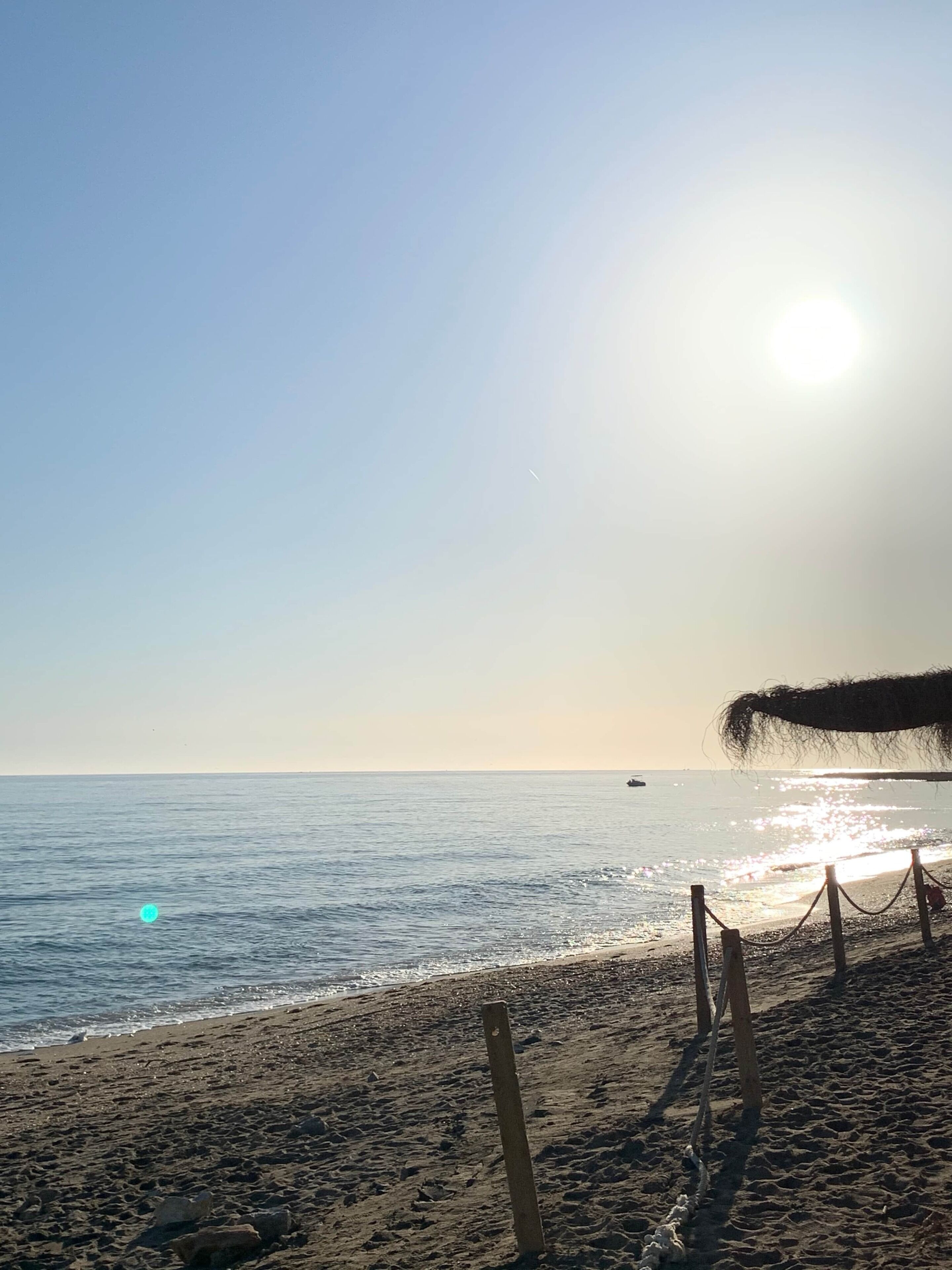 Una playa con cielo despejado, mar tranquilo y una valla de madera.