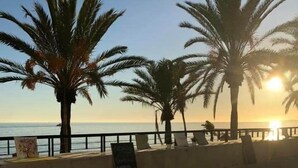 Eine Küstenpromenade mit Palmen, blauem Himmel und der Sonne, die über dem Meer aufgeht oder untergeht.