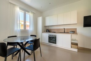 Eine moderne Küche mit weißen Schränken, einem eingebauten Backofen und einem Essbereich mit einem Glastisch und schwarzen Stühlen.