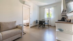 Un salón moderno y minimalista con sofá, una mesa de comedor con sillas, una zona de cocina con microondas y una ventana con cortinas.