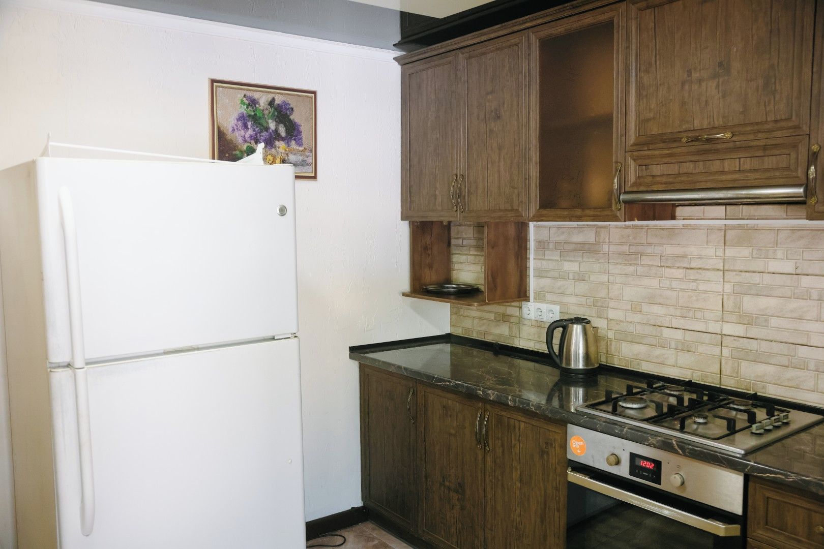 Una cocina compacta con un refrigerador blanco, gabinetes de madera, una encimera negra y una estufa a gas.