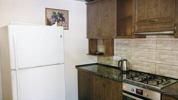 Una cocina compacta con un refrigerador blanco, gabinetes de madera, una encimera negra y una estufa a gas.