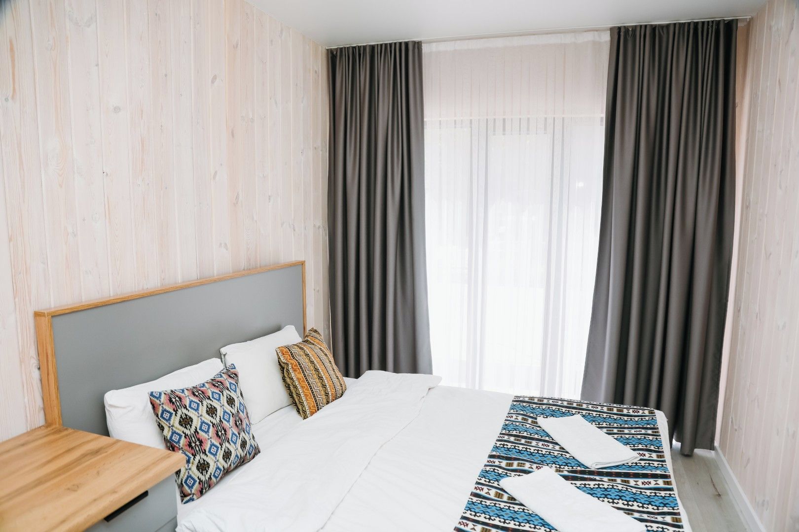 A hotel room with a bed, a nightstand, and a window with curtains.