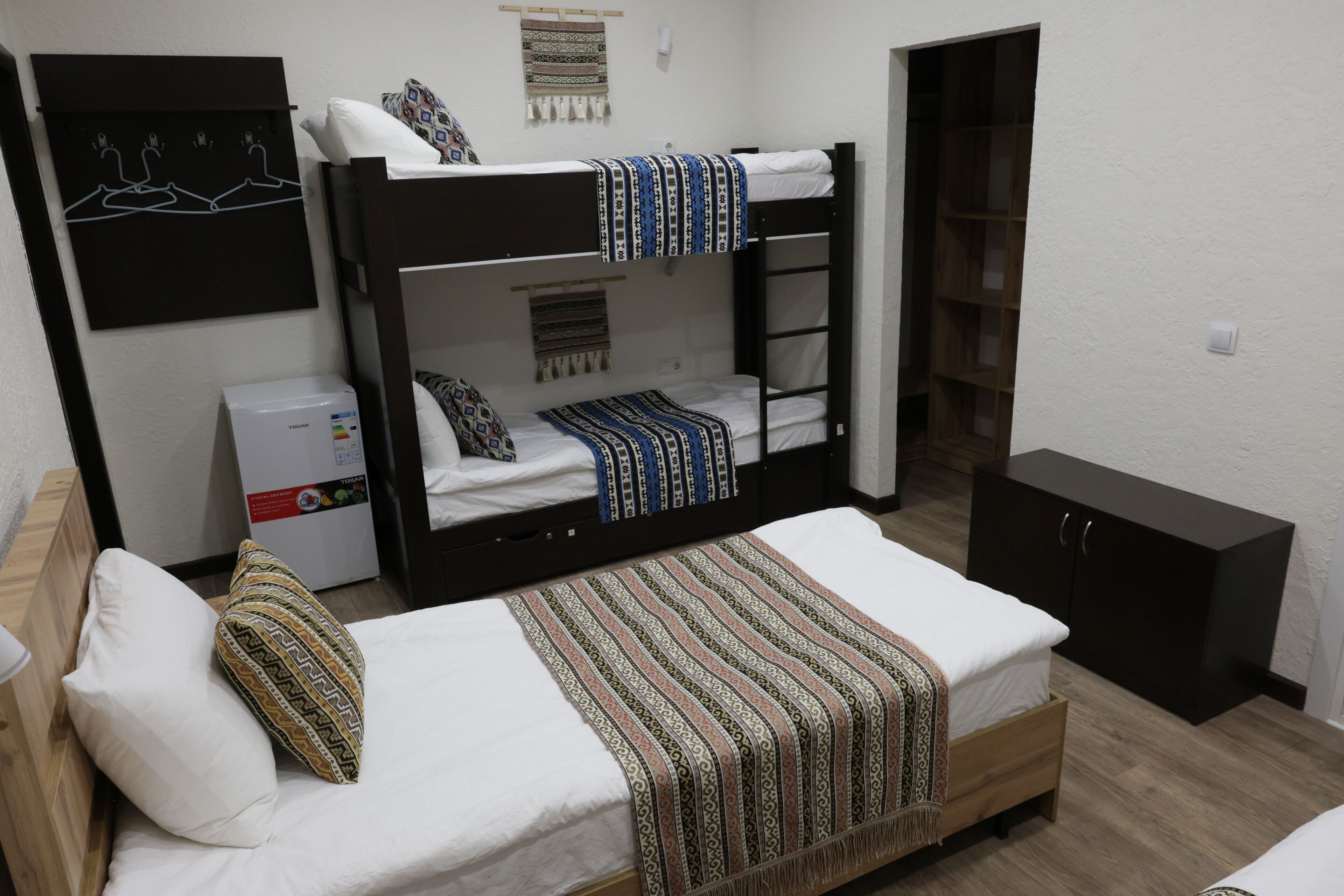 A bunk bed room with a desk, a refrigerator, and a wardrobe.