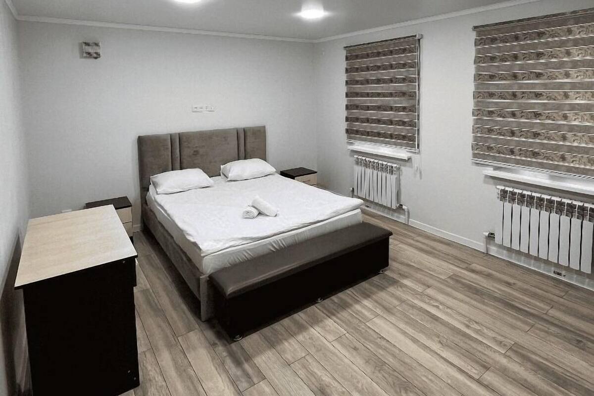 Un dormitorio con cama, mesitas de noche, radiador y ventana con persianas.