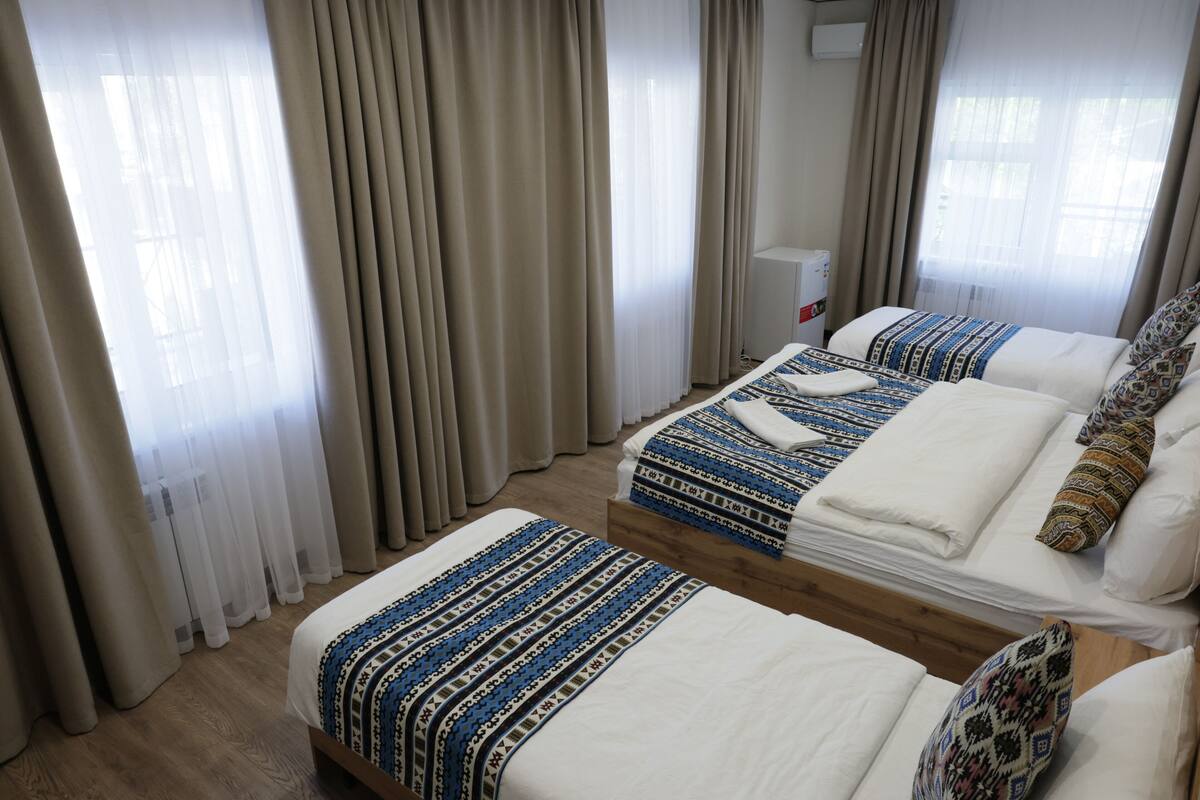 Habitación de hotel con dos camas, cortinas color crema, radiador blanco y suelo de madera.