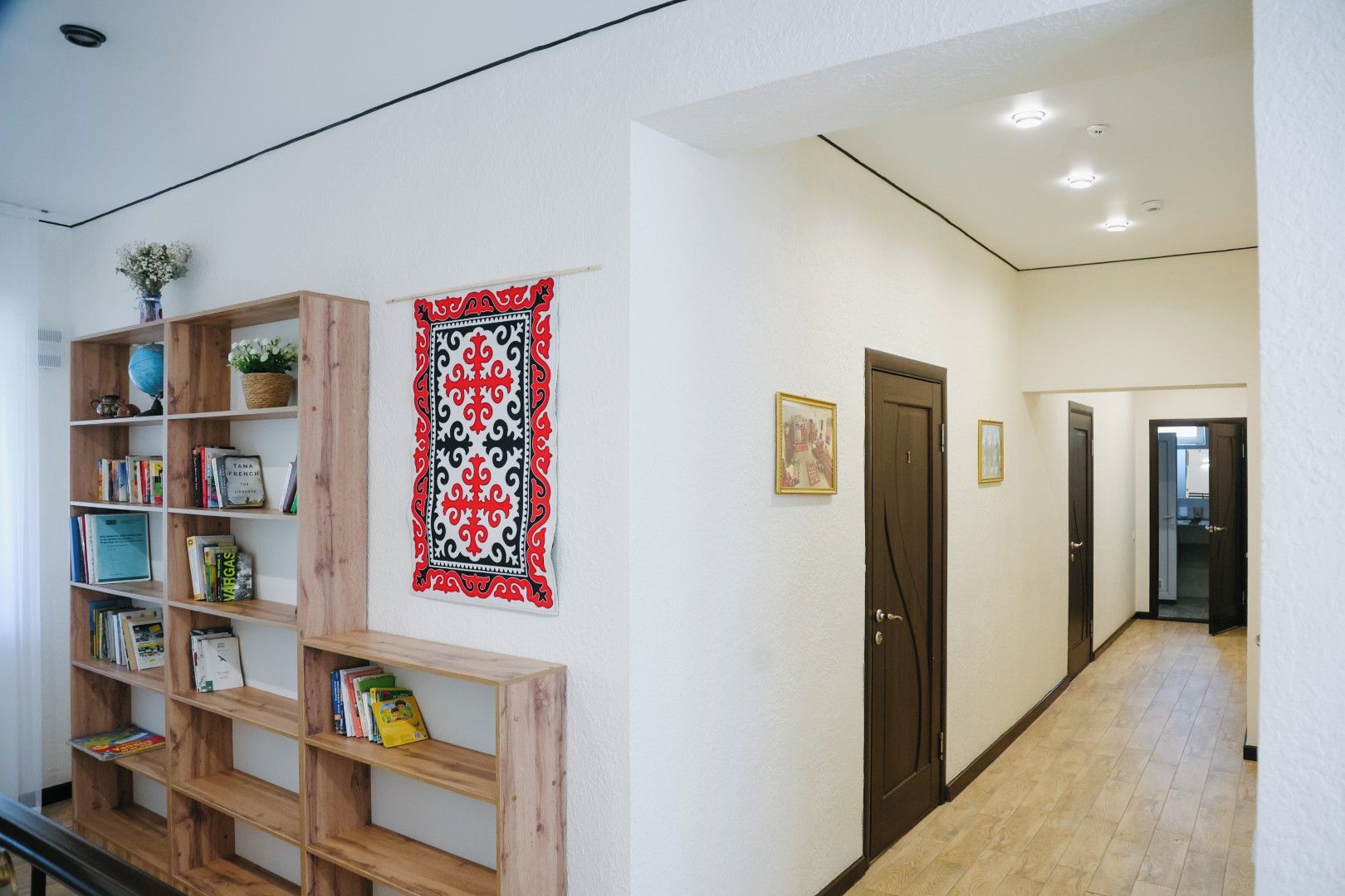 Un pasillo con una estantería de madera, un tapiz decorativo y una puerta que da a otra habitación.