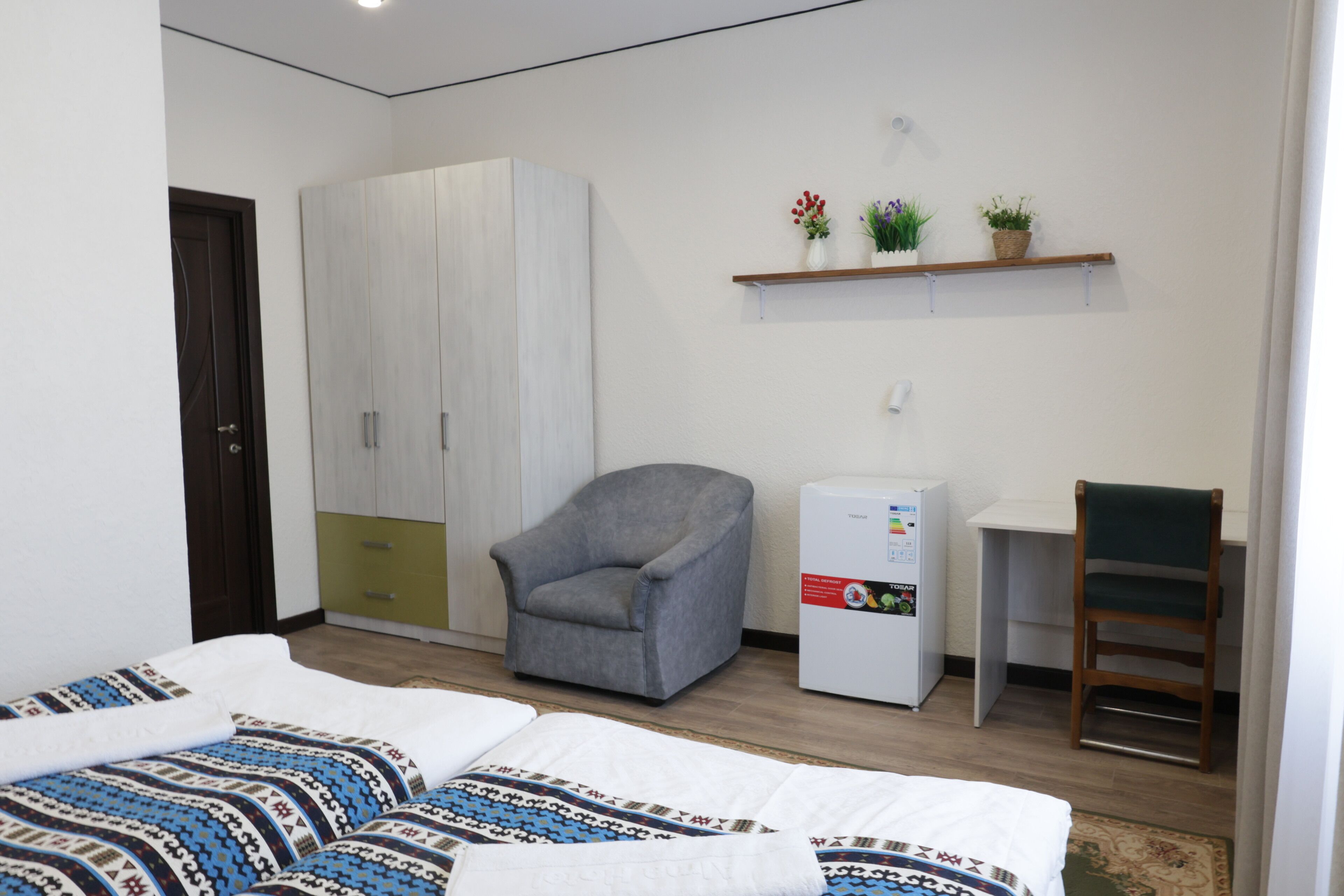Een slaapkamer met een bed, een kledingkast, een bureau, een stoel en een koelkast.