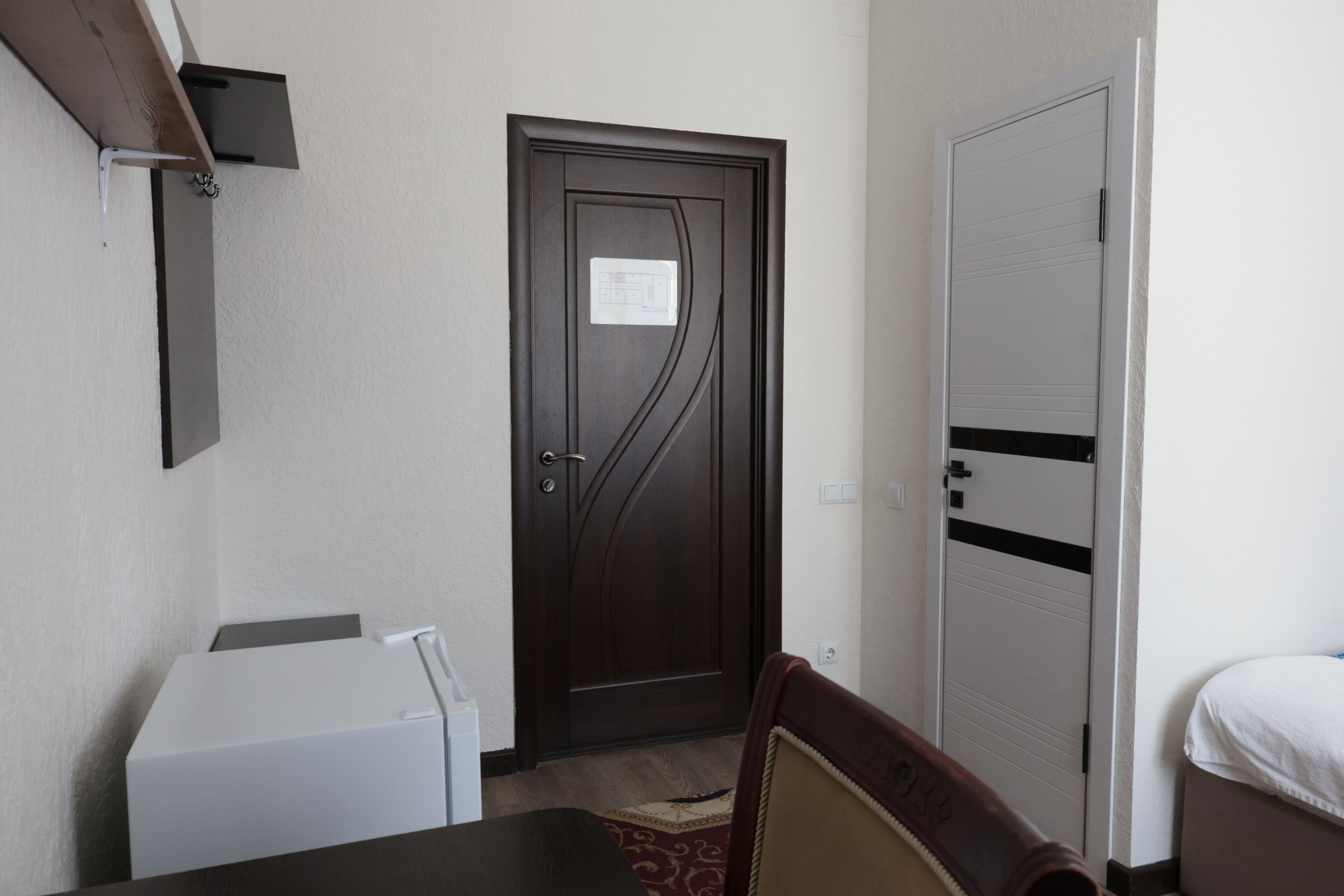 A room with a dark wooden door, a white bed, a small table, and a chair.