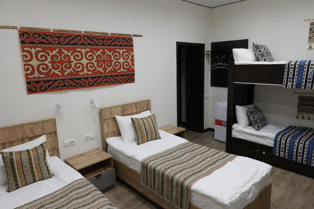 Habitación de hotel con dos camas individuales, una litera, un cabecero de madera, un tapete estampado y un adorno en la pared.