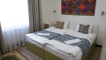 A bedroom with a bed, a nightstand, a wall tapestry, and a window with curtains.
