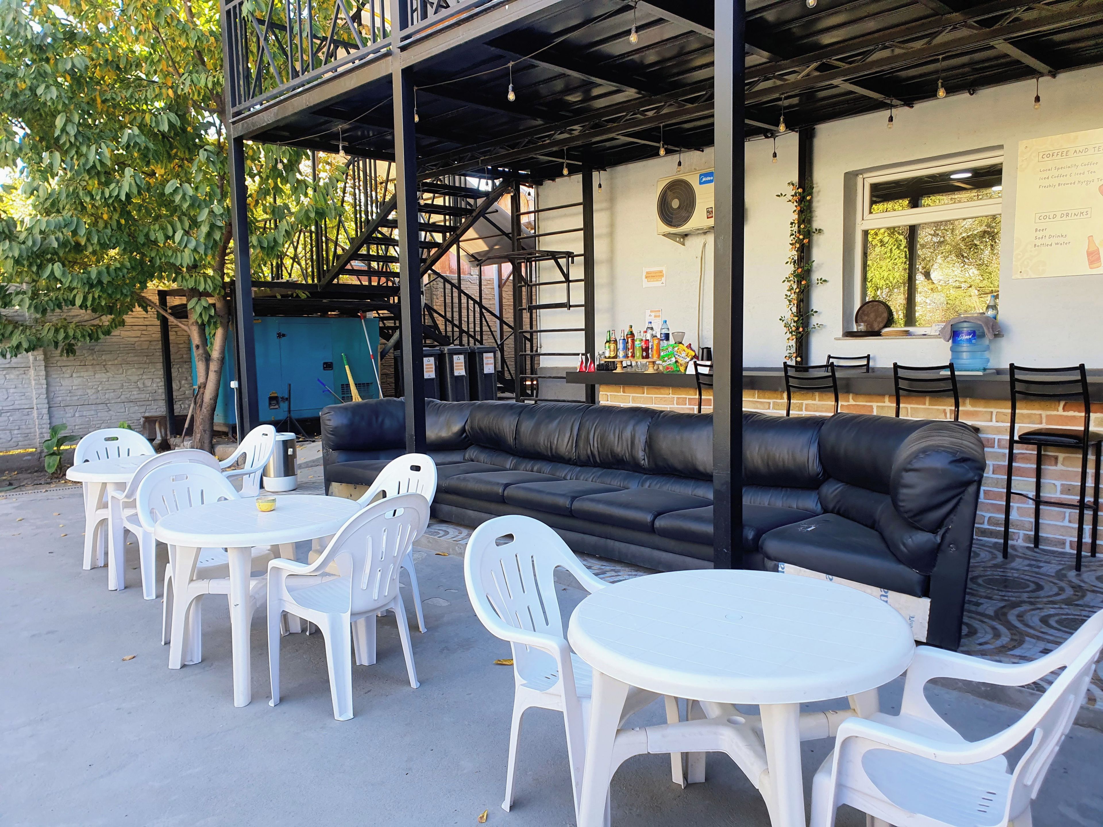 An outdoor seating area with a black leather couch and white plastic chairs, a bar with a menu, and a staircase leading to an upper level.