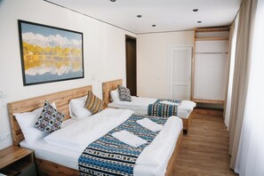 Habitación de hotel con dos camas, cabecero de madera, un cuadro en la pared y una puerta que da a otra habitación.