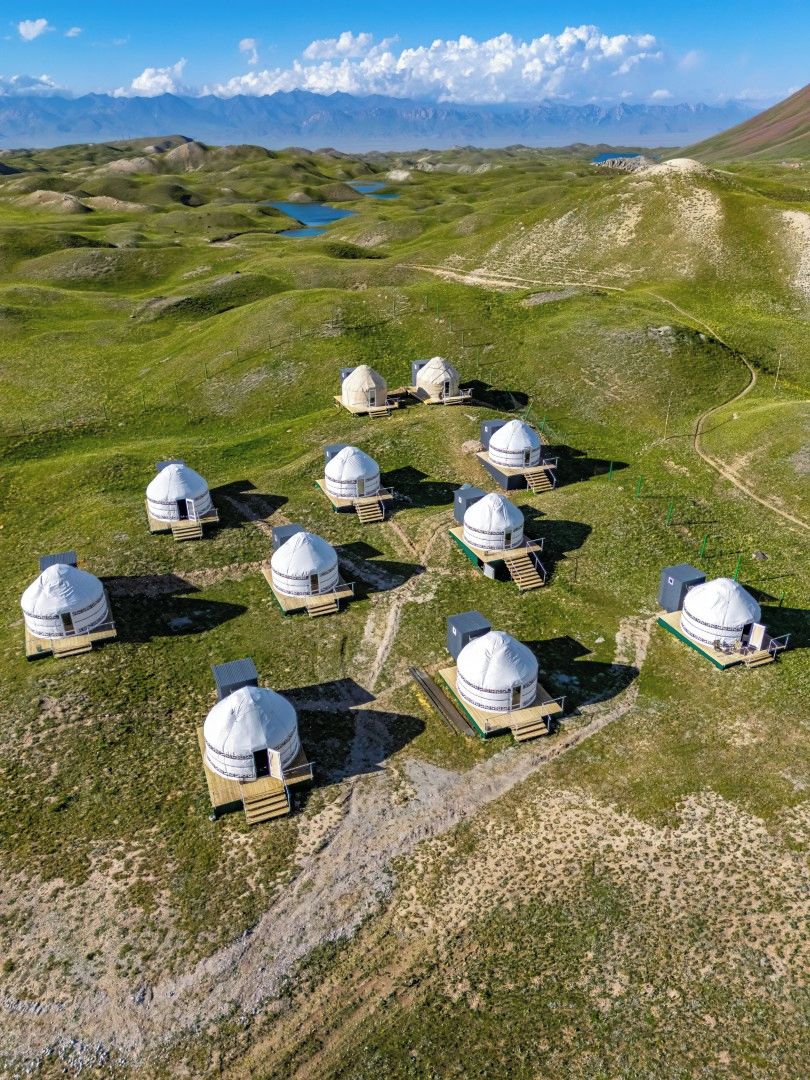 A series of dome-shaped structures with solar panels, arranged in a circular pattern on a grassy terrain with a mountainous backdrop.