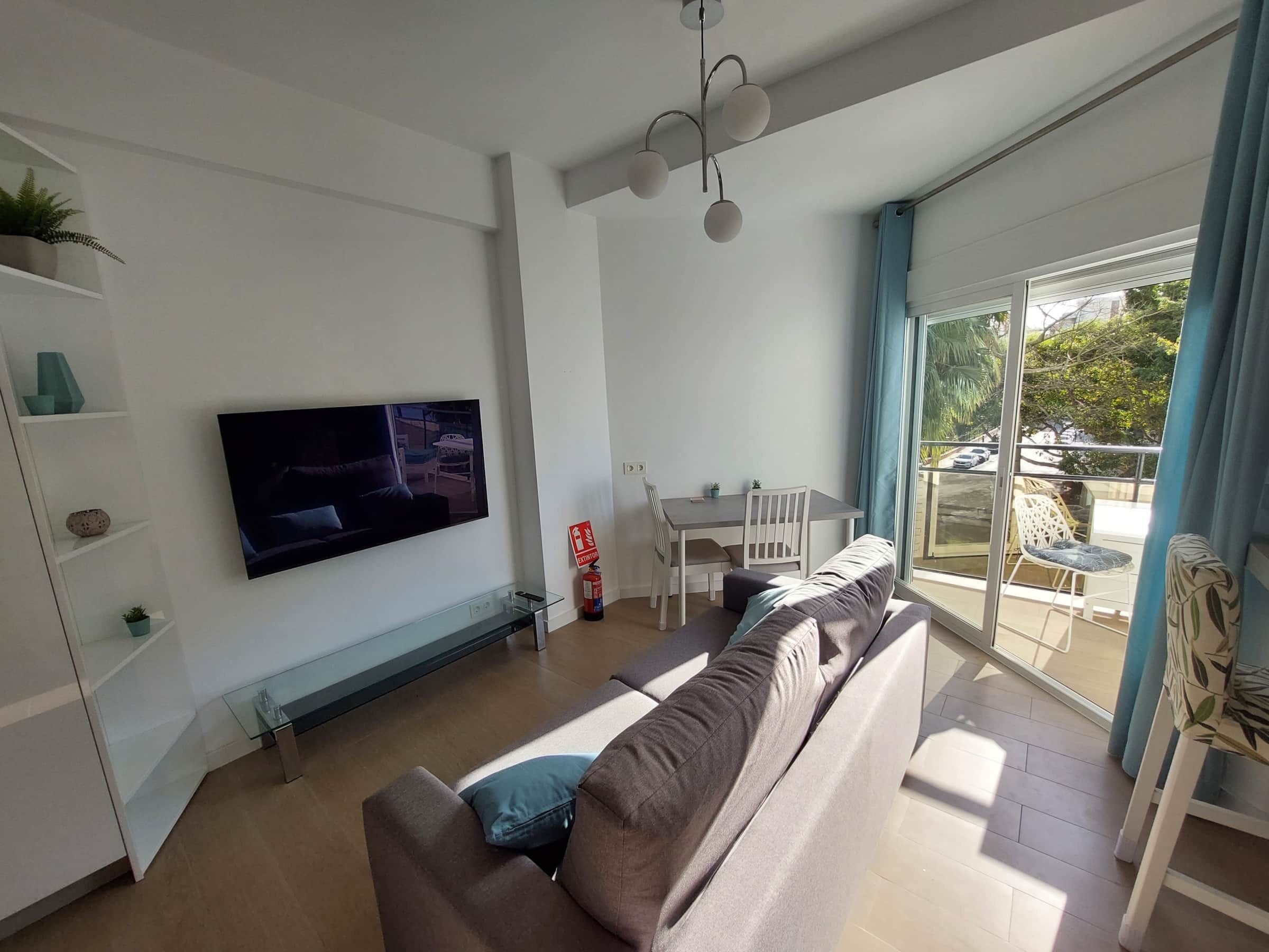 Un salon moderne doté d’un téléviseur à écran plat, d’un canapé, d’une table à manger et d’un balcon aménagé avec du mobilier d’extérieur.