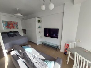 Ein modernes Wohnzimmer mit Bett, Sofa, Fernseher und kleinem Tisch.