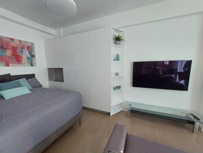 Ein modernes Schlafzimmer mit einem Bett, einem Fernseher, einem Glastisch und einer Zimmerpflanze.