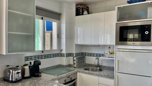 Una cocina con armarios blancos, encimera de granito, tostadora, hervidor, fregadero y microondas.