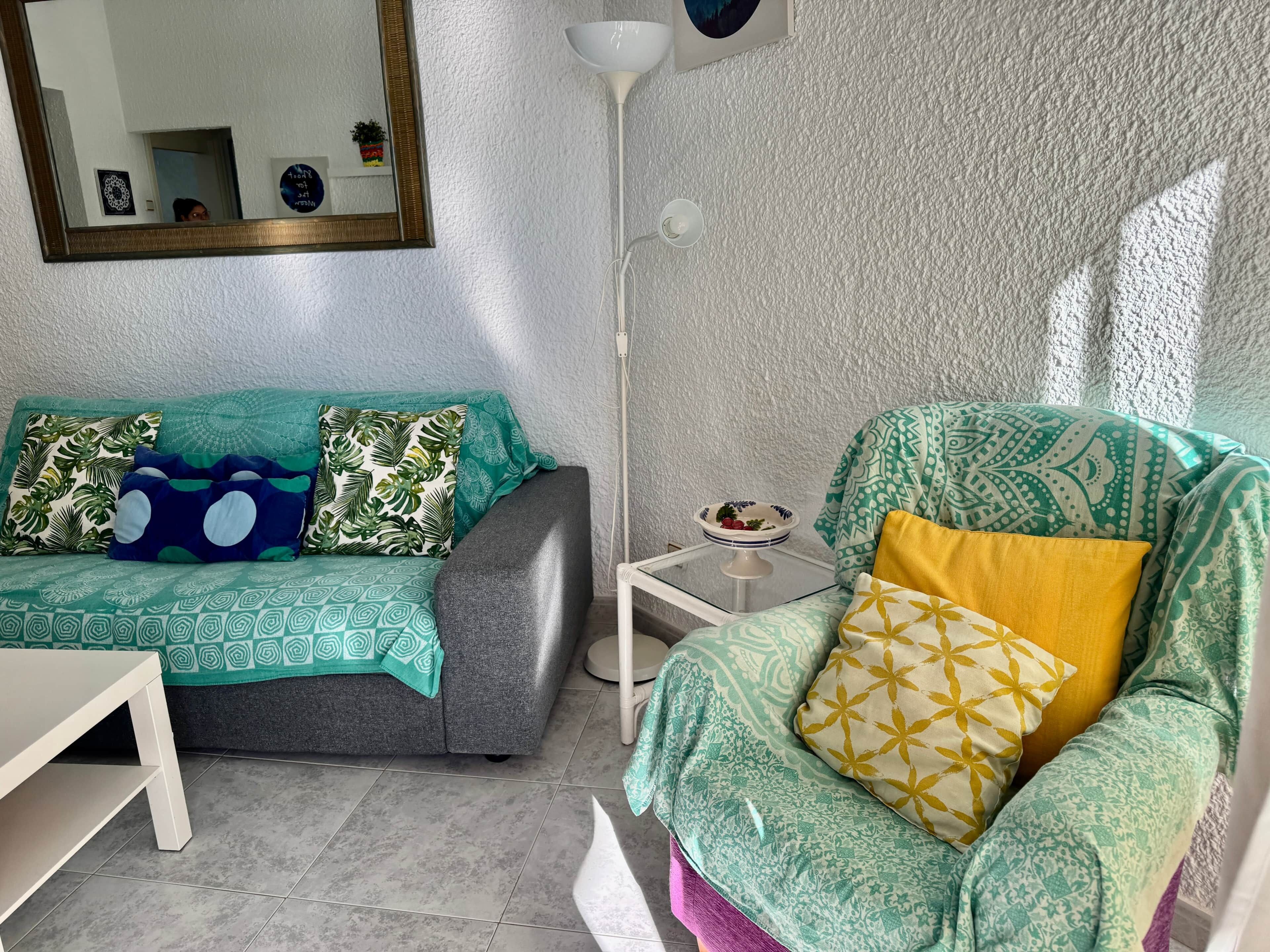 Ein Wohnzimmer mit grauem Sofa, einem grünen Sessel, einem weißen Beistelltisch und einer Stehlampe.