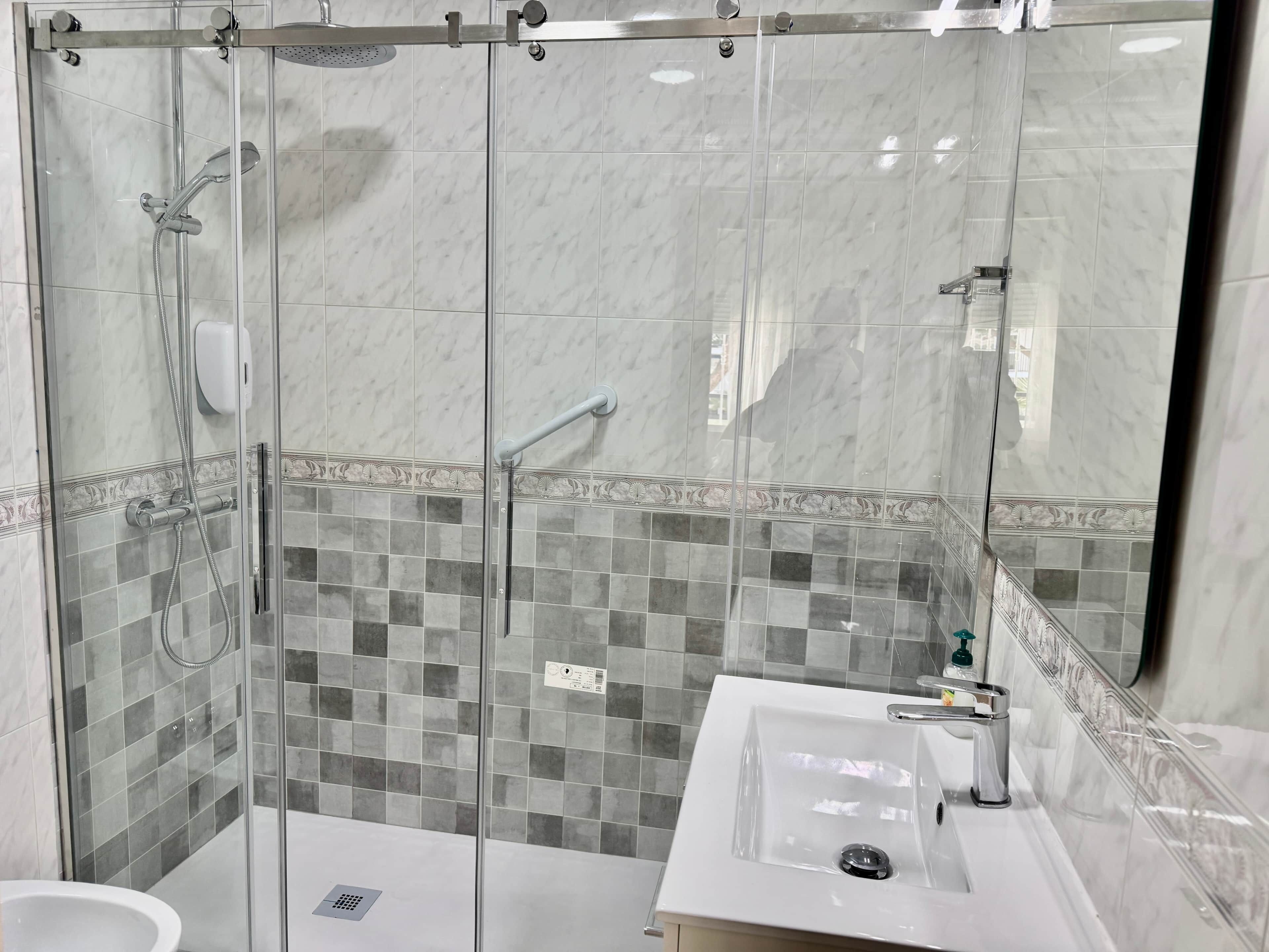 Ein modernes Badezimmer mit einer gläsernen Duschkabine, einem Waschbecken inklusive Spiegel und gefliesten Wänden.