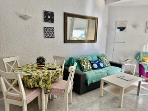 Ein Wohnzimmer mit einem Esstisch, Stühlen, einer Couch, einem Couchtisch und einem Spiegel an der Wand.