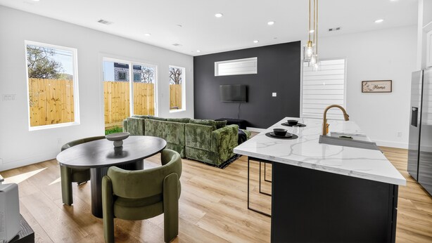 A modern kitchen with a central island, a dining area with a round table and chairs, and a living area with a sofa.