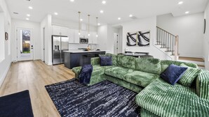 A modern living room with a green sofa, a black and white rug, and a kitchen in the background.