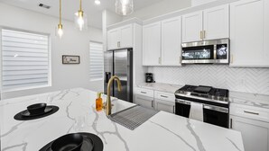 A modern kitchen with white cabinetry, stainless steel appliances, and pendant lighting.