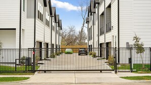 A gated residential area with white buildings, a clear sky, and a green car parked in the driveway.