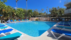 A swimming pool with blue water, surrounded by lounge chairs and palm trees. - Wahoo Watch Two Bedroom Condo (Stock Island)