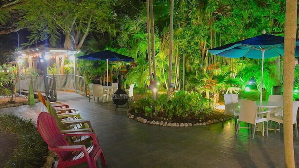 An outdoor patio area with chairs and tables, surrounded by lush greenery and illuminated by ambient lighting. - Wahoo Watch Two Bedroom Condo (Stock Island)