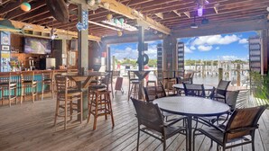 An outdoor bar area with wooden furniture, a TV screen, and a view of the water. - Barracuda Bay Two Bedroom Condo (Stock Island)