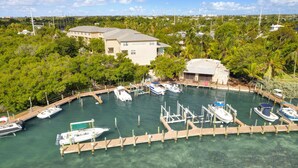 A marina with several boats docked, surrounded by lush greenery and a building with a sloped roof. - Barracuda Bay Two Bedroom Condo (Stock Island)