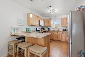A kitchen with wooden cabinets, a granite countertop, a stainless steel refrigerator, and a bar stool area. - NEW! Coastal Oasis in Surfside Beach (Surfside Beach)