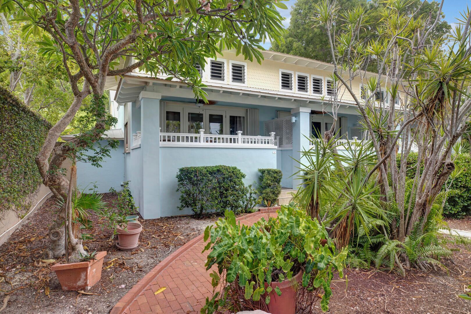 A two-story house with a light blue exterior, a covered porch, and a brick pathway leading to the entrance.