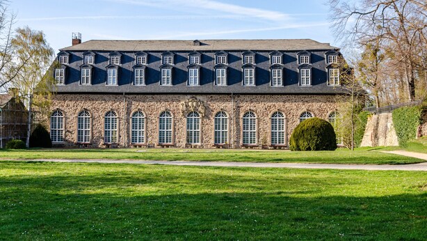 Un grand bâtiment en pierre, doté de nombreuses fenêtres en arc de cercle et d’une façade symétrique.